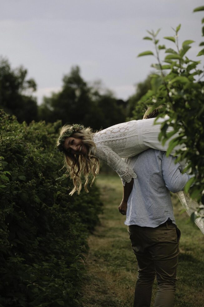 The groom is carrying his bride through a raspberry farm.